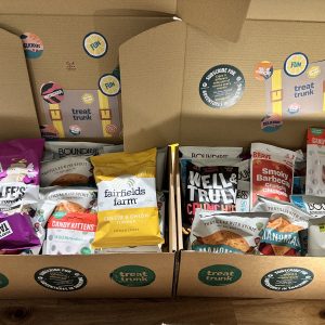 Two open Full Treat Trunk boxes packed with full-size healthy snacks from small UK makers: Metcalfeโs popcorn, Fairfields Farm crisps, Boundless, Candy Kittens, Well&Truly and more